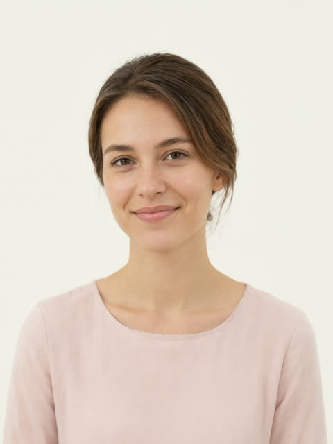 Portrait of a smiling young woman with tied-back hair, head and shoulders, against a bright plain background